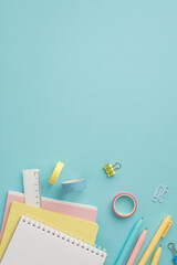 School accessories concept. Top view vertical photo of colorful stationery stack of notebooks pens adhesive tape ruler and binder clips on isolated pastel blue background with copyspace