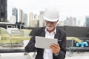 Wall Mural - An old elderly engineer man or worker, people working in industry factory, using a tablet technology device. Chiller tower on rooftop building. System work machine. Condenser pipe lines.