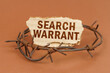 On a brown surface, barbed wire and a cardboard sign with the inscription - Search warrant