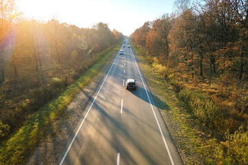 Canvas Print - Aerial view of intercity road with fast driving cars between autumn forest trees at sunset. Top view from drone of highway traffic in evening