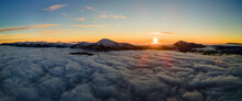 Aerial View Of Vibrant Sunrise Over White Dense Clouds With Distant Dark Mountains On Horizon