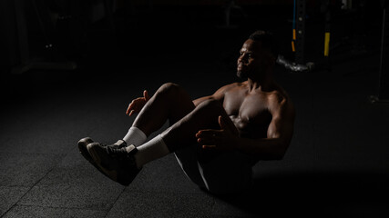 Afro american man doing abdominal exercises in a dark studio. 