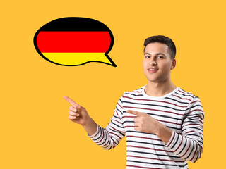 Canvas Print - Portrait of young man pointing at speech bubble on yellow background. Concept of speaking German