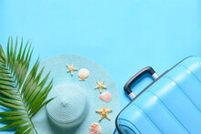 Suitcase, Straw Hat, Palm Leaf And Seashells On Blue Background