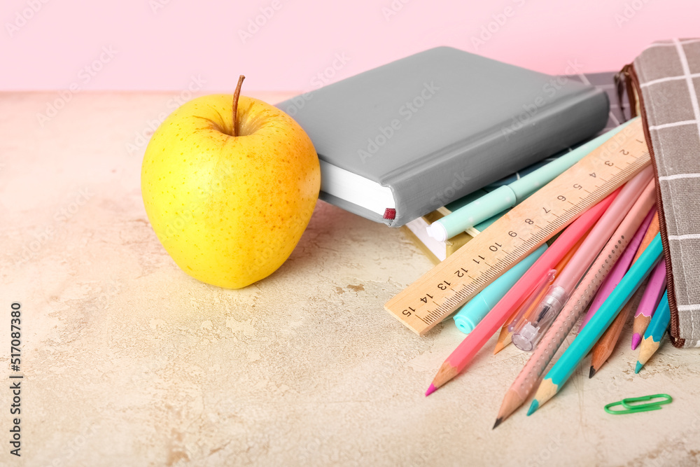 School stationery with apple on table against pink background