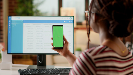 Poster - Company employee looking at smartphone display with greenscreen, doing remote job at home. Using isolated chroma key copyspace with blank mockup template and mobile phone background.