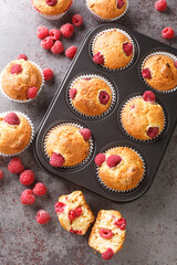 Wall Mural - Summer raspberry muffins with white chocolate close-up in a muffin pan on the table. Vertical top view from above