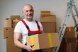 Leinwandbild Motiv Middle-aged man mover in uniform holding cardboard box, portrait