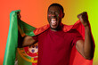 Portrait of african american male football supporter with flag of portugal over orange lighting