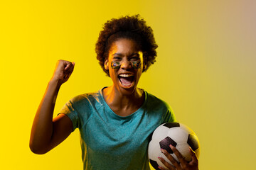 Image of african american female soccer fan with flag of brazil cheering in yellow lighting