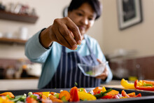 Low Angle View Of Biracial Mature Woman Garnishing Fresh Vegetables Salad In Kitchen