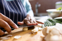 Midsection Of Biracial Mature Woman Chopping Garlic Cloves On Cutting Board In Kitchen