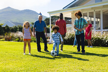 Multiracial Multigeneration Family Looking At Boy Playing Soccer On Grassy Field In Yard In Summer