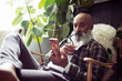 © Caia Image - Mature man with beard using smart phone in armchair