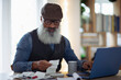 © Caia Image - Mature man with beard budgeting at laptop