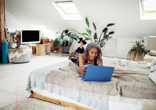 Senior Woman With Credit Card Paying Bills At Laptop On Bed