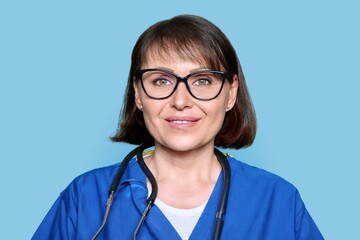 Wall Mural - Middle aged female nurse in blue uniform with stethoscope smiling looking at camera