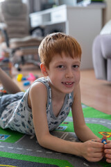 Young child boy plays constructor at home on the floor. Preschool education. Home fun. Lying on the carpet smiling at the camera