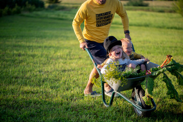 Happy father and his children playing with a wheelbarrow on a sunny autumn day