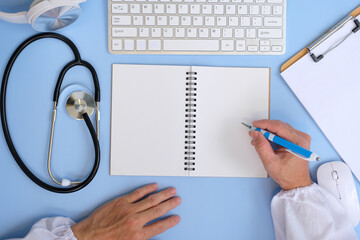 Poster - Doctor sits at her desk in an office, writing a prescription. Write something on a blank notebook page while a physician is writing in a medical file in the clinic. top view work space