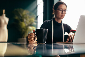 Wall Mural - Female dressmaker working on laptop with cup of coffee