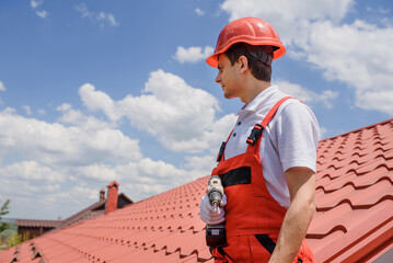 Wall Mural - Man worker master in red overall and helmet is fixing the metal tile roof.