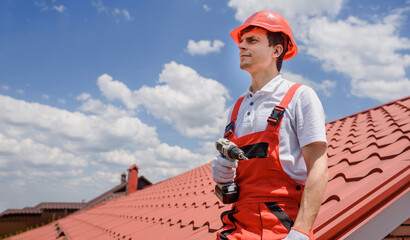 Wall Mural - Man worker master in red overall and helmet is fixing the metal tile roof.