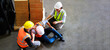© NVB Stocker - Top view. First Aid and safety first. Engineering talking on walki talki radio to employee while his warehouse coworker lying unconscious at industrial factory. Health insurance emergency accident.