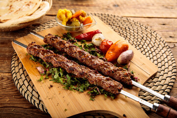 Wall Mural - Adana Kebab served in a wooden cutting board isolated on wooden background side view