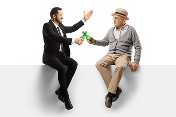 Poster - Elderly man and a happy businessman sitting on a blank panel and toasting with bottles of beer