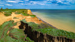 Ruined clay slope by the sea. Cracked clay cliff on the coast. A crumbling and cracked clay wall on the beach.