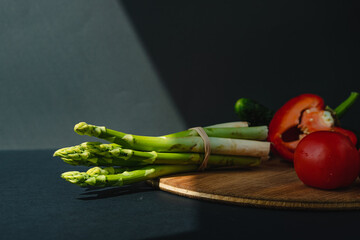 branches of fresh green asparagus, peppers and tomatoes on a wooden board, dark gray background, top view. Basic trend concept with copy space.