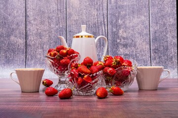 Canvas Print - On wooden table are three vases filled with ripe strawberries, coffee pot and two mugs of coffee.