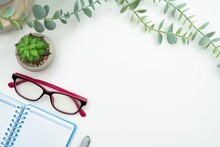 Top View Of An Open Notebook And Glasses On A White Background With Green Plant And Copy Space