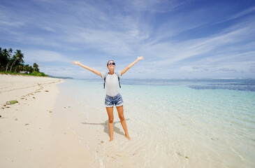 Poster - Vacation and freedom. Happy young woman rising hands up standing on tropical beach enjoying beautiful view.