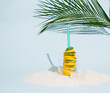 © Andjela - Glass filled with lemon and mint leaf with straw for refreshing summer drink placed on sand and decorated with ice cube and palm leaf. Minimal creative cocktail summer on bright blue background.