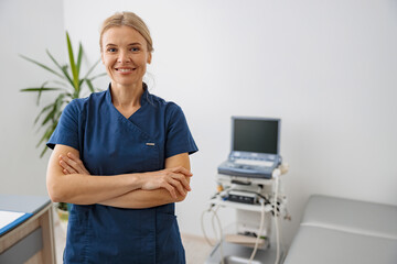 Wall Mural - Smiling doctor, ultrasound specialist looking at camera on her workplace in clinic