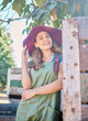 © Jade M/peopleimages.com - Portrait of a woman in a straw hat standing under a tree next to a rustic wooden crate. One young happy female wearing a summer hat and dungaree dress in a garden on a sunny day picking apples