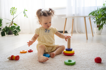 Eco friendly plastic free toys for toddler. Little girl making her first step while playing alone with modern natural wooden pyramid with rings. Stylish simple wooden toys for child concept