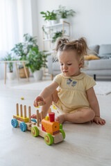 Active girl. Vertical shot of the baby playing with wooden developing toys alone at home. Eco-friendly wooden toys for children. Happy childhood concept