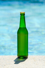 A Bottle Of Cold Beer Stands By The Pool On A Hot Summer Day. Vertical Format.