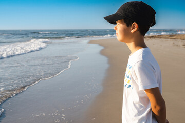 Wall Mural - Young boy wearing a cap standing alone and looking out to sea