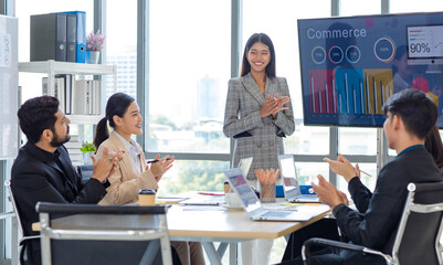 Businesswoman manager presenter in formal suit standing holding pen pointing at graph chart document on whiteboard presenting company information to Asian male female colleagues in meeting room