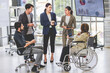 Group of millennial multinational multicultural Asian Indian businessmen and businesswomen with disabled handicapped partner sitting on wheelchair taking coffee break discussing together in office