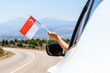 Woman holding Singapore flag from the open car window driving along the serpentine road in the mountains. Concept