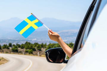 Wall Mural - Woman holding Sweden flag from the open car window driving along the serpentine road in the mountains. Concept