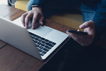 Poster - Man working on laptop and using mobile phone with digital tablet on wooden table at coffee shop, telecommuting