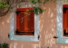 Bright Fancy Orange Summer House With Garden And Wooden Closed Shutters, Shadows On Wall In Hot Summer Day