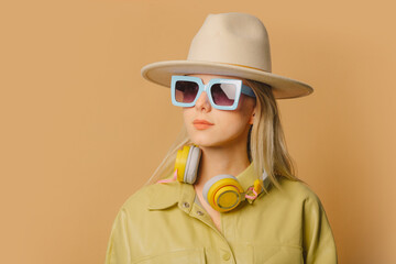 Poster - Stylish 80s woman in eyeglasses, headphones and hat on brown background