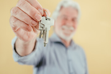 Defocused senior agent man holding keys of new house apartment rent buy sell